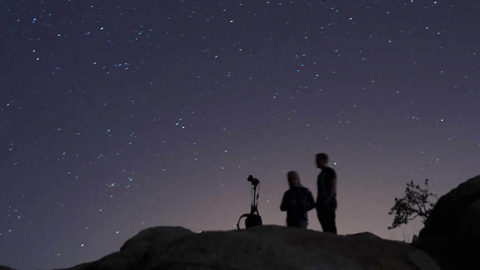 Two people stand with a telescope against the night sky.