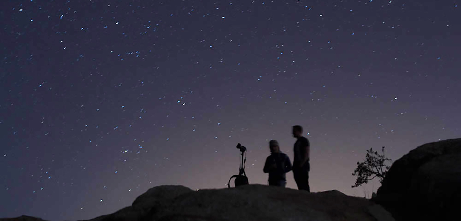 Two people stand with a telescope against the night sky.