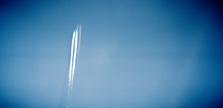 Jet taking off with contrails behind it seen through a window.