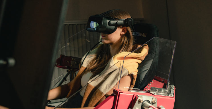 Woman wears VR headset while sitting in simulator.