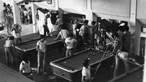 Black and white photo of students shooting pool and playing arcade games