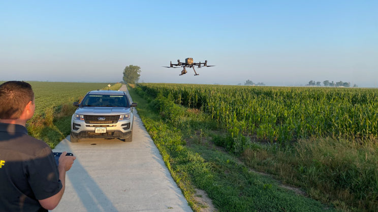 Deputy Jason Grubbs pilots a drone over a field of corn with a sheriff's SUV nearby