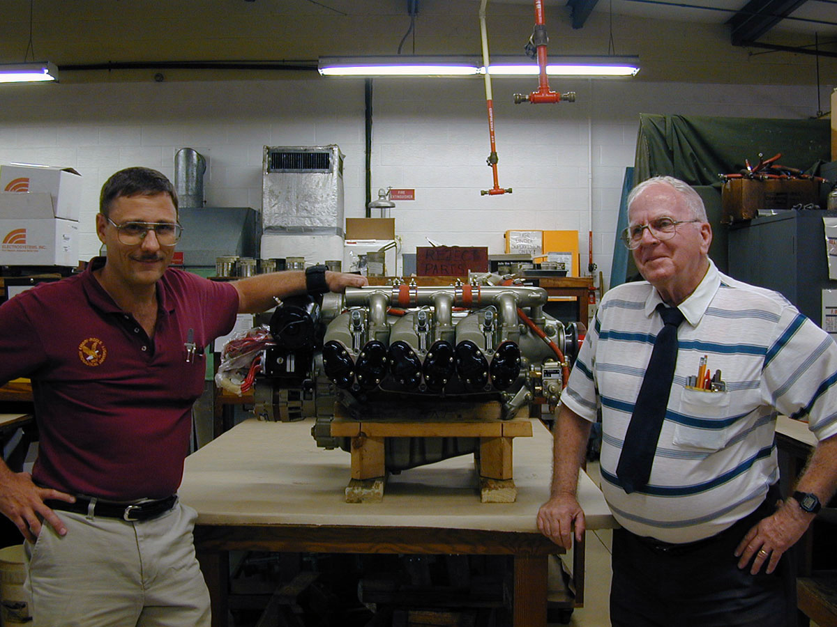 Sonnenfeld (’86, DB), AMS repair station operations lead instructor and engine repair station manager, left, and Professor Emeritus Chandler "T" Titus, right, stand next to a freshly completed engine in the repair station at the Daytona Beach Campus.
