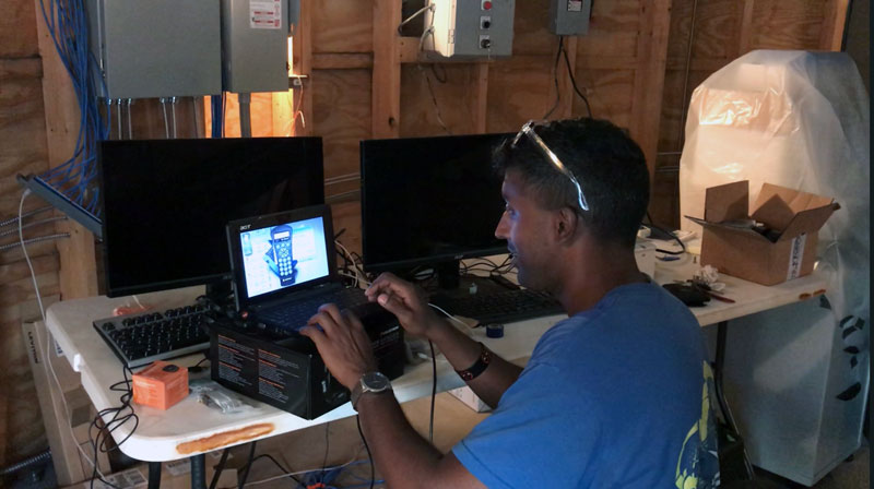 Michael Nayak sitting at a desk with a small laptop, testing the remote automation functions of the LANDIT telescope.