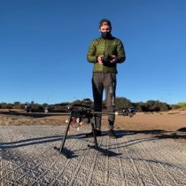 Matthew Robinaugh in an open field standing near a multi-rotor drone on the ground