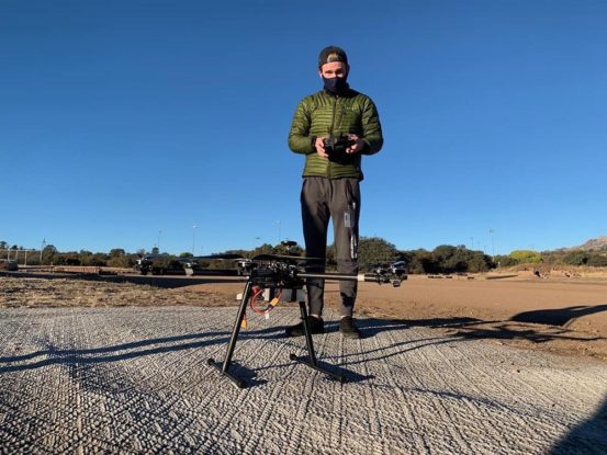 Matthew Robinaugh in an open field standing near a multi-rotor drone on the ground