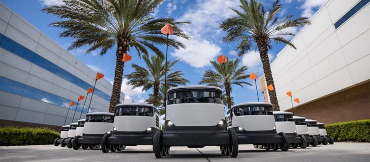 Multiple small delivery robots in a row on a paved pathway
