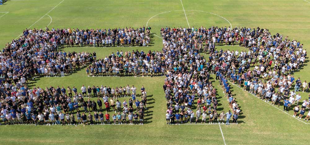 hundreds of students on soccer field in shape of letters ER