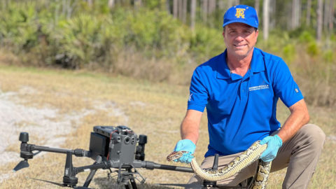 Researcher holds a python with a drone sitting beside him