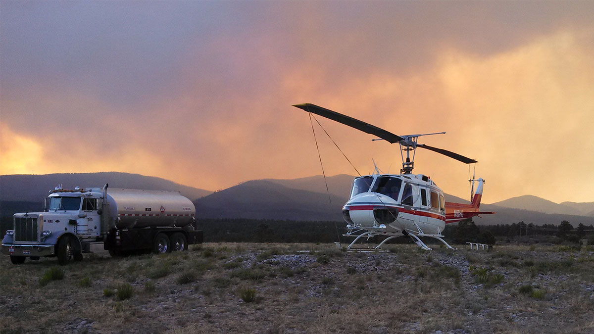 Huey on a remote helibase next to a fuel tanker truck, with a wildfire in the background