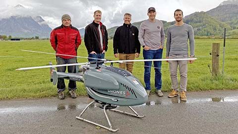 Five men standing by a large drone helicopter.