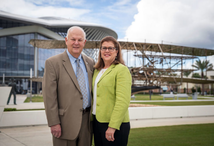 David and Karen O'Maley standing in front of the Wright Flyer statue at the Daytona Beach Campus.