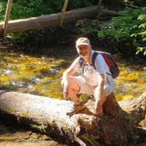 Warren Childers kneeling on a tree trunk over a river