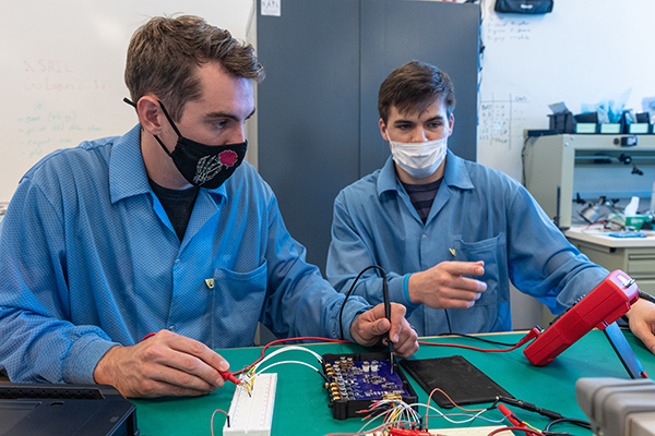 Two students work on electronic panel