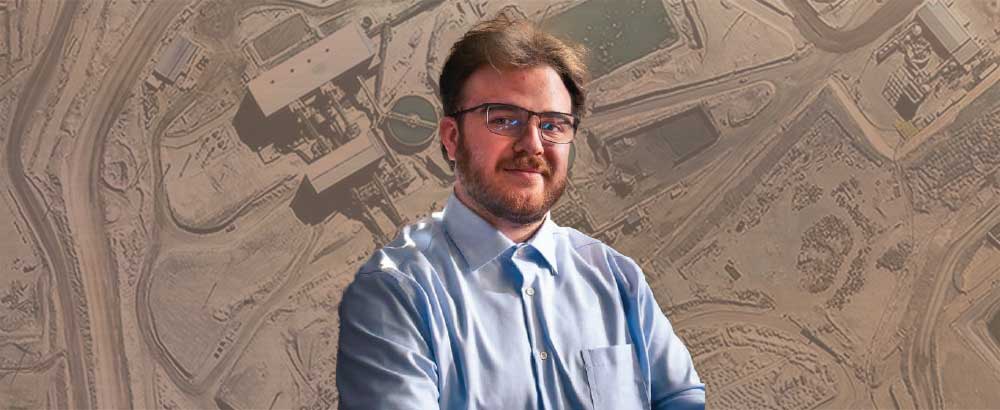 Riley Grant stands in front of aerial image of building in the desert