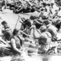 black and white photo of a large group of men on inflatable boats paddling hard in every direction